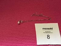 Full view of the 14k gold chain necklace with pearl pendant, laid flat on a textured pink surface, showing chain length and clasp.