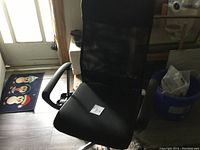 Front and side view of black modern office chair with mesh back and cushioned seat, placed indoors near a door and window.