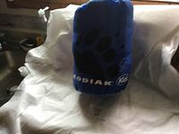 Photo showing the blue cylindrical storage sack with black paw print and Kodiak branding containing the kids sleeping bag.