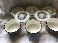 Front view of 6 ceramic soup bowls with 5 clear plastic lids placed on top, showing various patterns and interior colors.