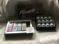 Photo showing Pinnacle Gold box for 15 golf balls, open box of used Titleist golf balls, and boxed set of mixed new golf balls.