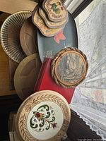 Photo showing multiple wooden serving trays and cork hot pads stacked on top of each other near a window.