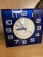 Square Mid Century Modern desk/table clock with blue frame and white Arabic numerals on face.