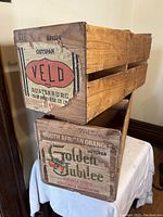 Side view showing the label on one crate marked 'Veld Ripenburg' and the other 'Golden Jubilee South African Oranges'. Wooden slatted construction shown.