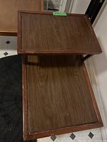 Photo showing two-tiered end table with wood grain surface and raised edge, with visible wear and scratches.