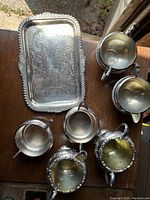 Photo showing three silver creamers and three sugar bowls with a detailed engraved silver rectangular tray.
