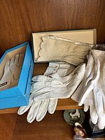 Four pairs of antique gloves displayed on a wooden surface including two pairs in blue boxes and two gloves laid out showing different textures.