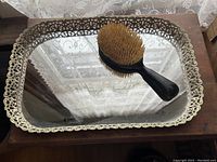 Rectangular mirrored tray with intricate metal border and large wooden handle brush on top