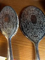 Close-up image of the back of the hand mirror and hair brush showing intricate floral and scroll engravings on silver surface.