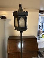 Full view of the black wrought iron floor lamp with castle style hexagonal lantern top and textured glass panels
