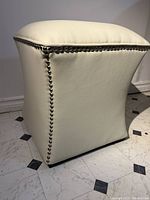 Side view of white leather Mid Century Modern stool showing curved shape and metallic stud detailing along edges.
