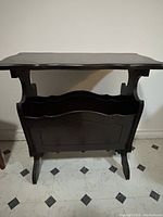 Front view showing rectangular top surface with slight lip and integrated lower magazine rack with wavy divider and inset panel detail.