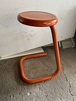 Full side view of orange tubular steel stool showing paper clip frame and round seat.