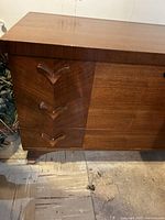 Front left corner view showing three carved V-shaped wooden handles on drawers and wood grain finish.