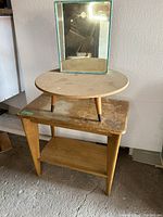 Round wooden table with three angled legs and a mirror on top, showing its shape and design.