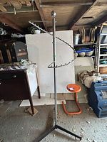 Full view of the upright chrome metal clothing rack with spiral hanger arm and tripod base in a storage area.