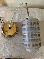 Side view of the cylindrical frosted glass ceiling light fixture with geometric blue and brown squares and brass-colored mounting plate, showing the white cord and metal rod.