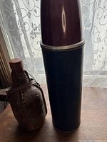 Photo of large vintage thermos bottle standing upright next to a small leather wrapped flask.