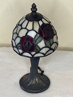 Small table lamp with stained glass rose patterned shade sitting on a beige surface against a cream wall.