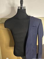 Front view of black tailor's fitting mannequin torso with a navy blue jacket sleeve draped on the right shoulder.