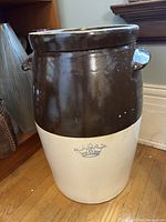 Full view of two-tone ceramic butter churn with a brown glossy finish on upper half and cream lower half. Crown stamp with number 6 visible on cream section. Two side handles.