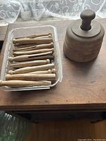 Vintage wooden clothes pins in a plastic case next to a wooden butter mold/press on a wooden surface with lace curtain background.
