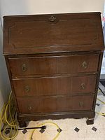 View of front of vintage wooden secretary desk with fold-down writing panel closed and three drawers below.