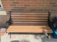 Front view of the wood bench with slatted seat and backrest, showing iron frame and armrests.