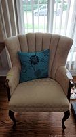 Front view of beige upholstered chair with blue floral pillow, showing chair design and condition