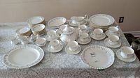 Full set on lace-covered table showing plates, cups, saucers, teapot and serving pieces