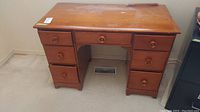 Front view of wooden desk showing the seven dovetailed drawers and top surface, with visible wear and scratches.
