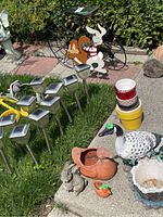 Photo showing metal bicycle plant stand decorated with painted rabbit and squirrel, ceramic goose planter, terracotta bird planter, ceramic rabbit, stacked flower pots, and solar stake lights on grass.