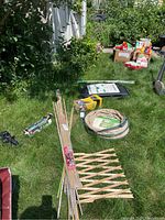 Full lot showing multiple gardening supplies arranged on grass including nylon container, bamboo stakes, garden hose, lattice fencing, composter base and various gardening accessories.