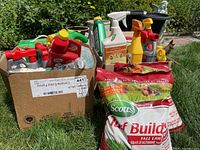 Photo showing two boxes with spray bottles, liquid fertilizers, and two red and green bags of Scotts Turf Builder Fall Lawn Fertilizer on grass background.