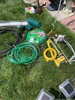 Multiple garden hoses, hose nozzle, hose fittings, and garden mesh laid on grass