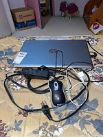 Overall view of HP Pavilion laptop with charger and wired mouse on a mattress.
