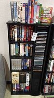 Wide shot showing three shelves filled with DVD and VHS movie cases plus tall rack of CDs stacked vertically.