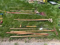 Full overview photo of garden tools laid out on grass showing rakes, pitchfork, hoes and edgers
