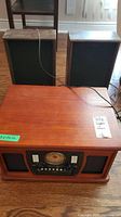 Wooden stereo console with two separate wooden speakers shown together on wooden floor. Audio cables visible.