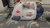 Side view of Bissell SpotLifter Spot Cleaner in white and blue sitting on carpet.