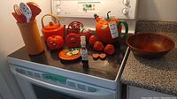 Overview of items arranged on a black stove top and the kitchen counter showing kettle, teapot, timer, faux fruit, utensil holder, and other items