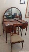 Front view of the vintage wood vanity with scalloped semi-circular mirror and wooden chair in front