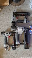 Three Husky air nailers laying on floor in used condition arranged side by side