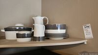 Shelf display of Block Spal 'Midnight' dishes including jug, lidded dish, bowls, and stacked plates with black geometric pattern.