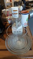Lot contents showing KitchenAid shredder, Betty Crocker hand mixer on table with Highmark ceramic vase and nine clear glass Duralex bowls stacked.