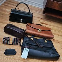 Overview photo showing all five items on wooden floor: black leather handbag, brown leather briefcase, black Normandie leather purse, multicolor small bag, and black coin purse