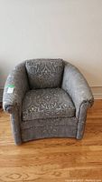 Front view of a gray patterned upholstered armchair with rolled arms and thick cushions