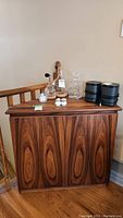 Front view of cabinet with bottles and glassware on top showing wood veneer grain and overall shape