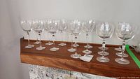 Seventeen clear crystal wine glasses arranged in a row on a wooden shelf or surface, showing the full set and their uniform design.