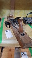 Large vintage wooden hand plane placed on wooden table showing front handle and adjusting blade mechanism.